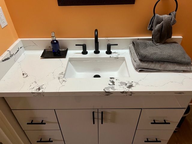 White bathroom vanity with black hardware, white countertop with gray veining, black faucet, and gray towels.