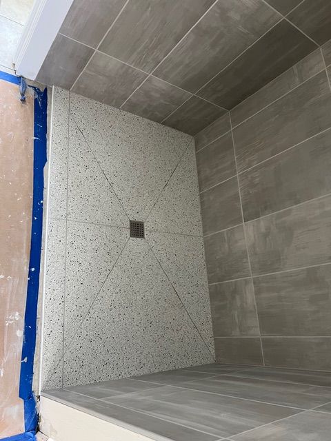 Newly tiled shower with gray walls and a terrazzo-style floor with a central drain.