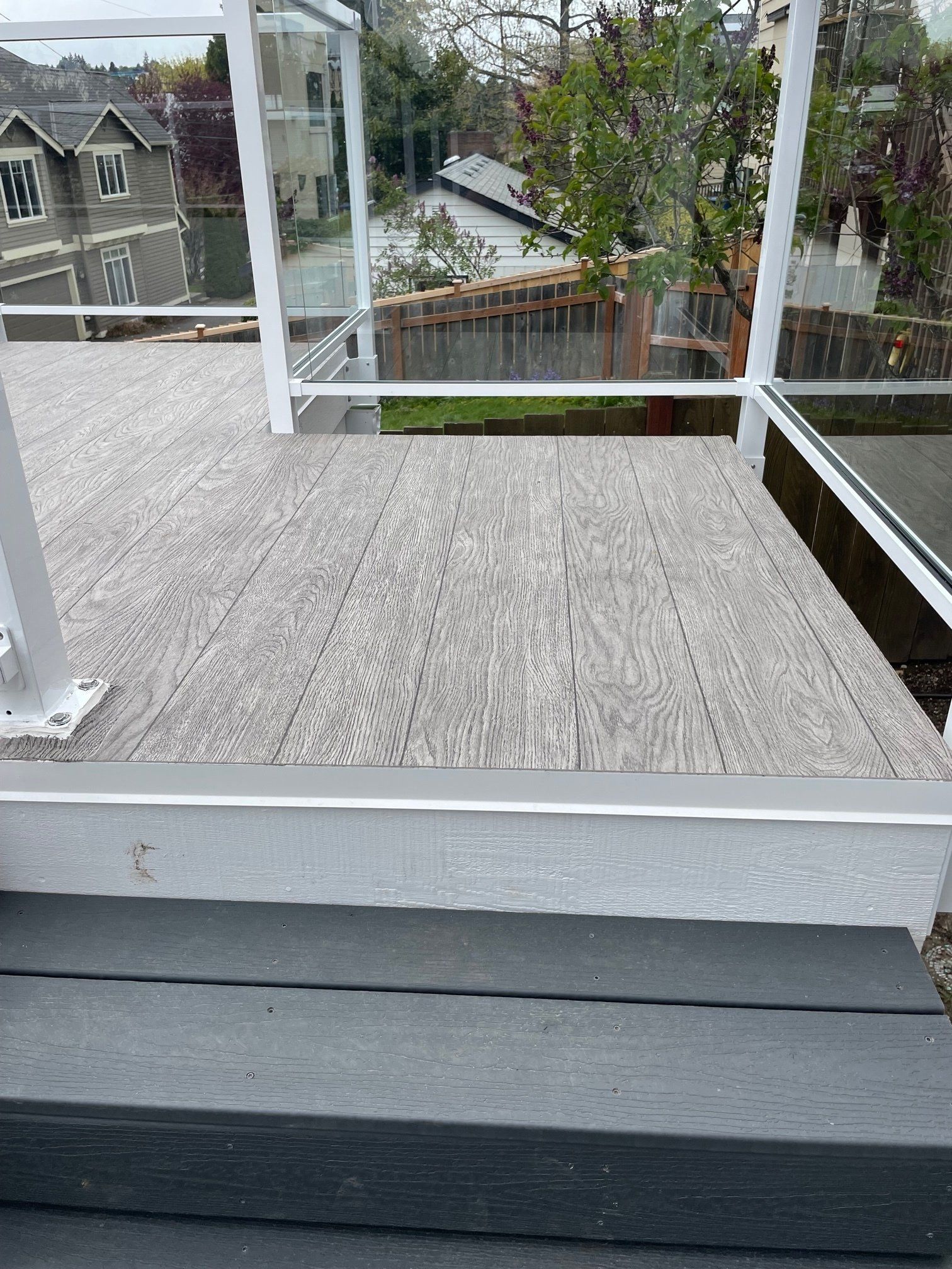 Composite deck with gray wood-look planks, white railing, and dark gray steps. View overlooking trees and houses.