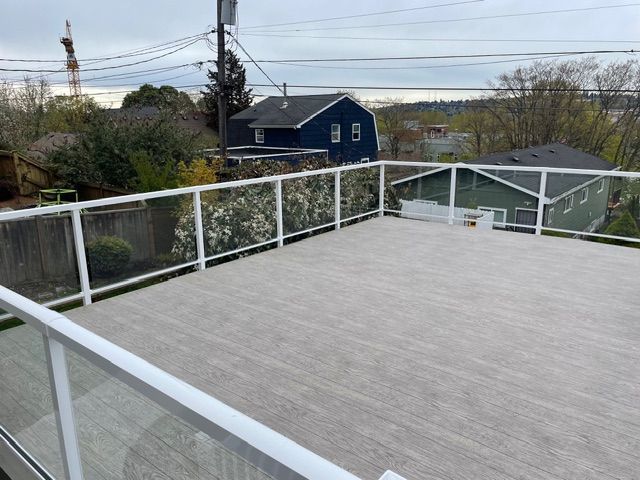 Large gray deck with glass and white railing, overcast sky. Houses and trees visible in background.