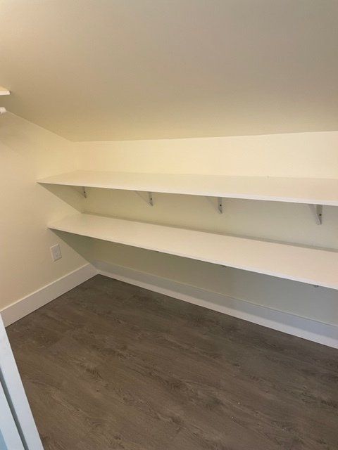 Closet with two white shelves against a beige wall, gray wood-look floor.
