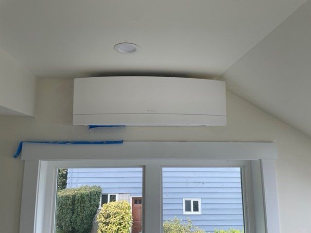 White wall-mounted air conditioner above a window. Blue tape below, with a light fixture and angled walls.