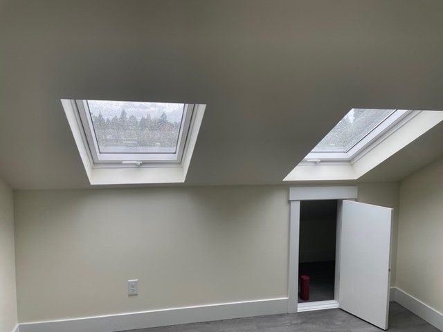 Two skylights and a white doorway in a room with light beige walls and a white baseboard.