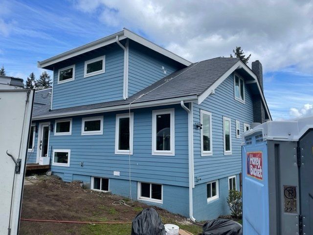 Blue house with white trim, new siding, windows. Portable toilet nearby, overcast sky.