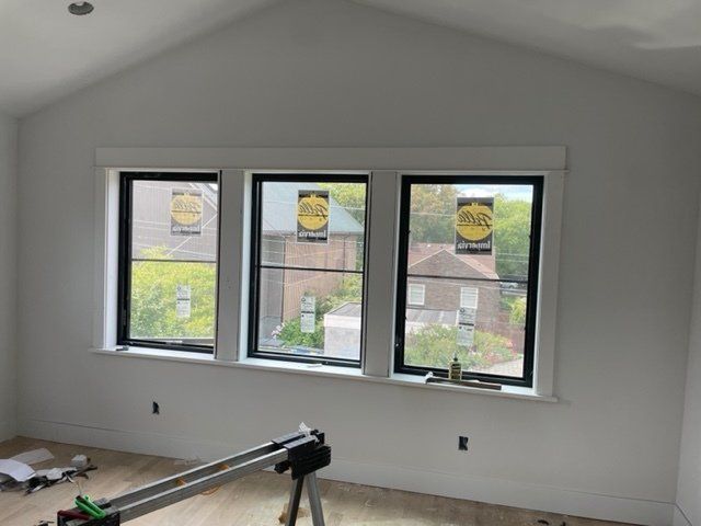 Interior room with three black-framed windows, white trim, and a vaulted ceiling. Construction materials are visible.