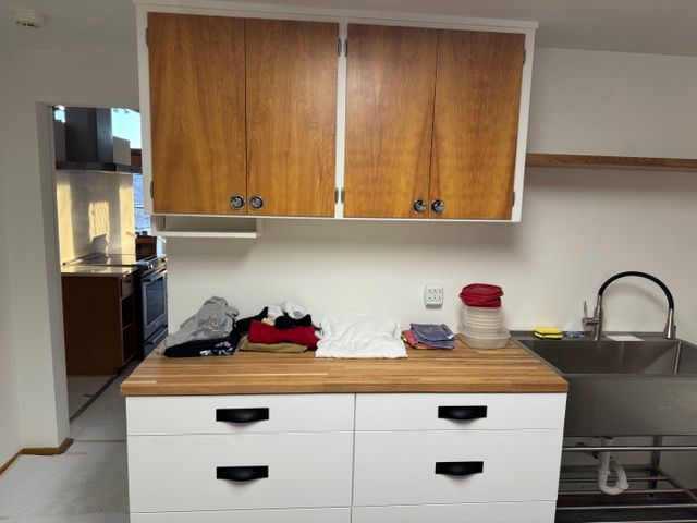 A small kitchen with upper wooden cabinets, white lower cabinets, a butcher block countertop, and a stainless steel sink.