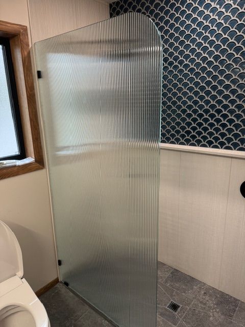 Shower with fluted glass panel, blue tile wall accent, and white toilet in a bathroom.