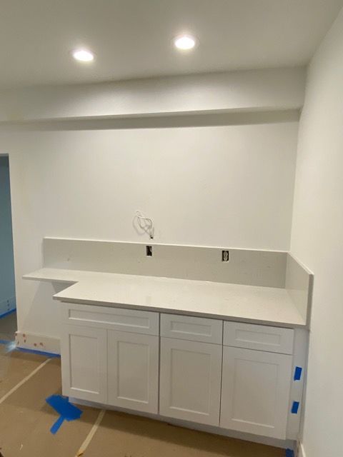 White cabinets with countertop in a room under construction. Electrical wires and outlets visible.