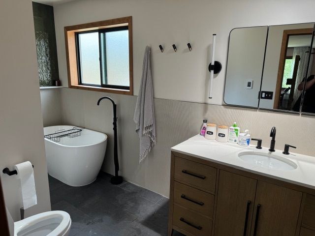 Modern bathroom with a white tub, vanity, and toilet; black fixtures; and neutral walls.