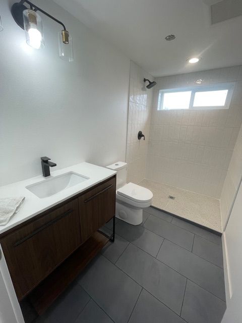 Modern bathroom with a dark wood vanity, white toilet and shower, and gray tile floor.