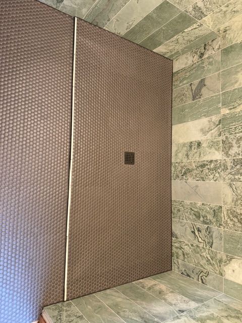 A shower with brown textured walls and green marble walls.