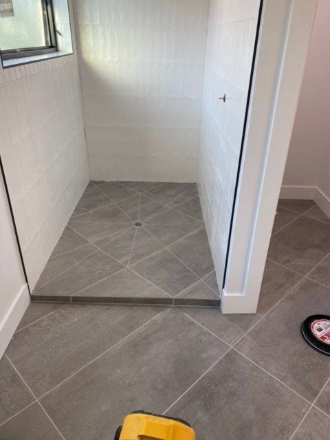 A tiled shower with a raised threshold, gray floor, white walls, and a drain.