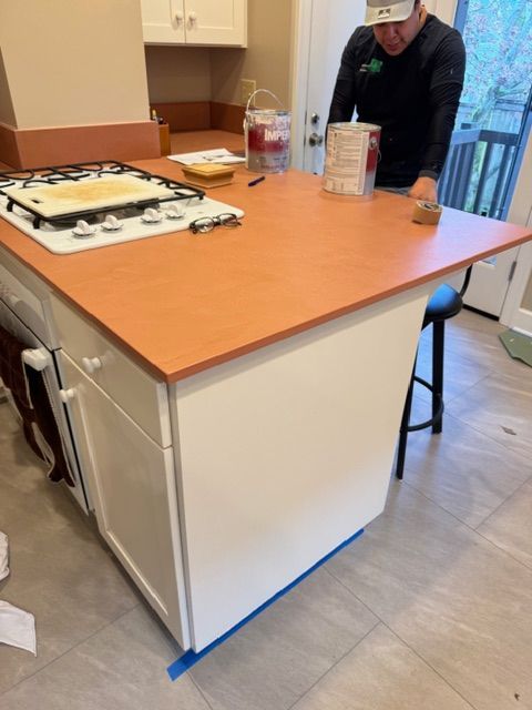 Person painting a kitchen island countertop orange with white cabinets.