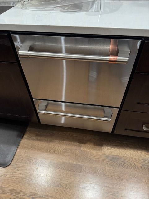 Stainless steel kitchen double drawer dishwasher with copper handle accents, installed under a countertop.