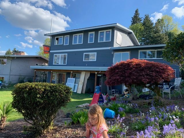 A blue house with multiple windows and a child in front of a colorful garden.