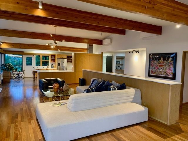 Open-concept living space with wood flooring, beams, a white sofa, and a partial wall separating it from the kitchen.