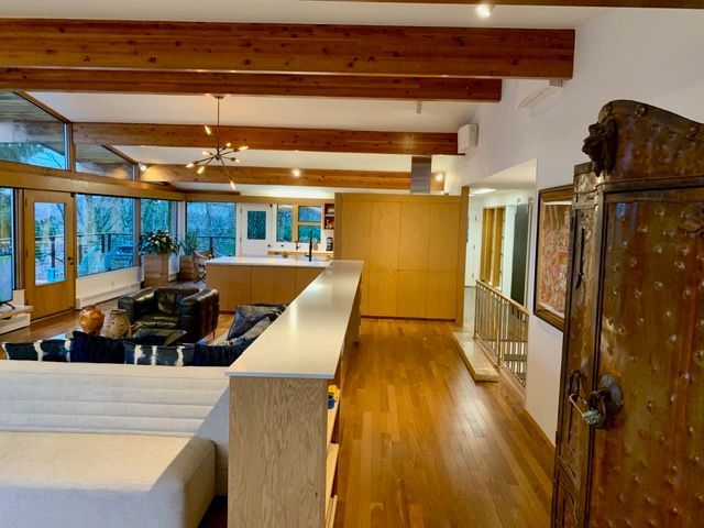 Spacious interior with exposed wooden beams, a kitchen, and a living area. Sunlight streams through large windows.