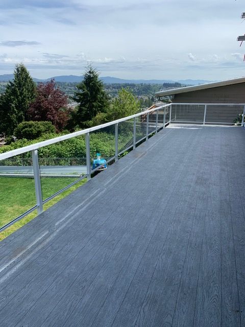 Deck with glass railings, overlooking a green landscape and distant mountains on a cloudy day.
