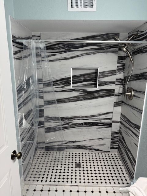 Bathroom shower with black and white marble walls and tile floor, and a built-in shelf.