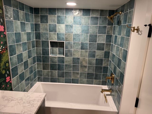 Bathroom with teal square tiles, gold fixtures, and white tub. Floral wallpaper visible on the left.