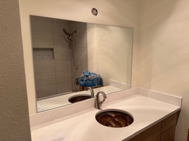 Bathroom vanity with rectangular mirror, white countertop, copper sink, and faucet; shower visible in the mirror.