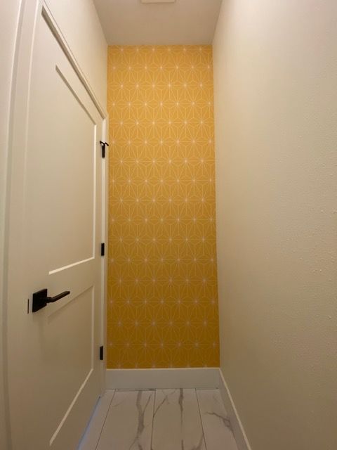 Narrow hallway with a yellow patterned accent wall, white door, and white and gray floor tiles.