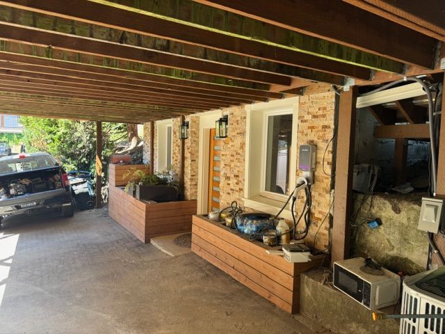 Covered porch with stone wall, wooden beams, planters, door, window, car parked on left.