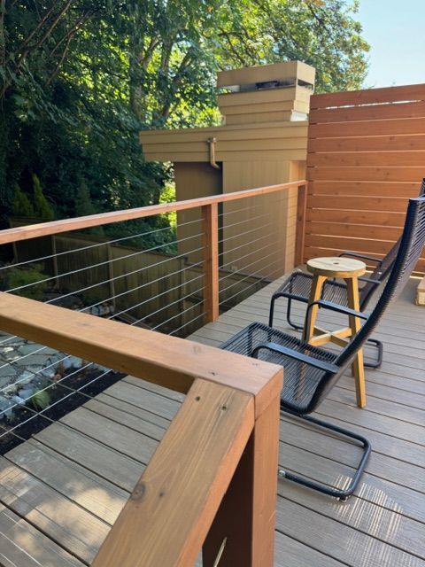 Wooden deck with a chair, small table, and cable railing, overlooking trees.