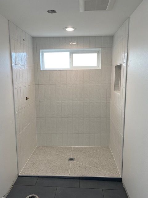 Finished white tiled shower with a small window, recessed shelf, and gray floor.