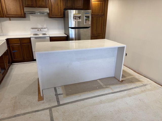 Kitchen with white island, dark cabinets, stainless steel refrigerator, and unfinished floor.
