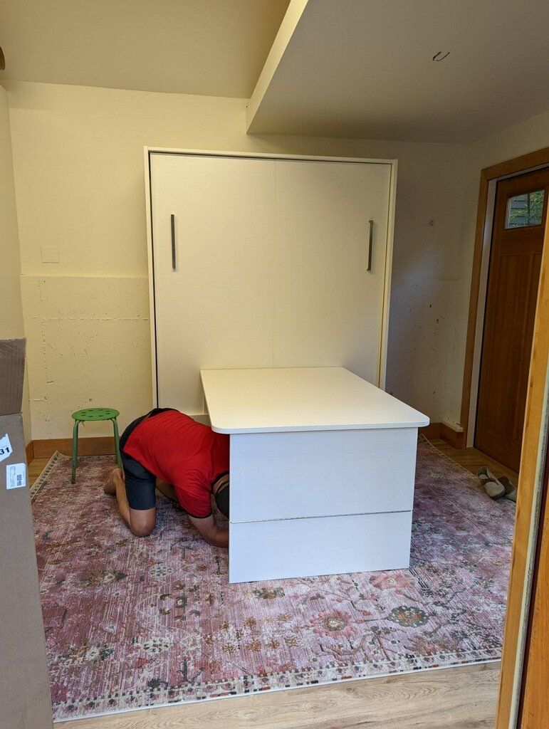 Person installing a white desk in a room with a white wall bed.