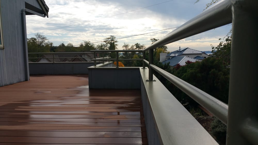 Wooden deck with stainless steel railings, overlooking a neighborhood under a cloudy sky.