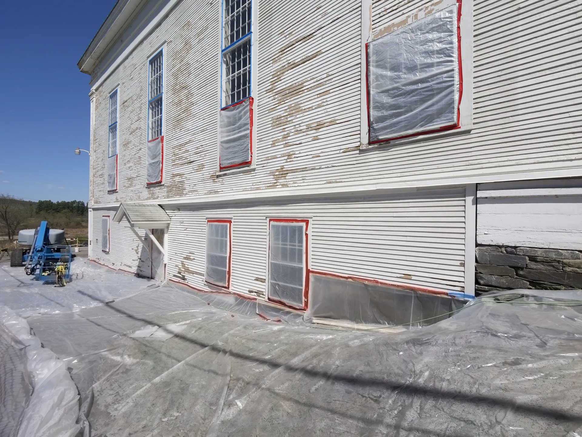A large white building is covered in plastic and is being painted.