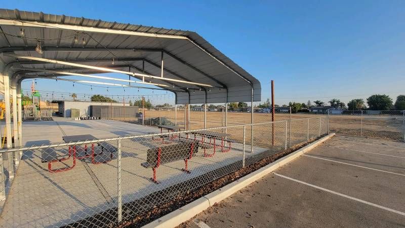 A picnic area with tables and benches under a canopy in a parking lot.
