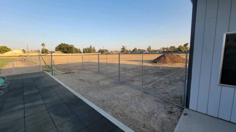 A chain link fence surrounds a dirt field next to a building.