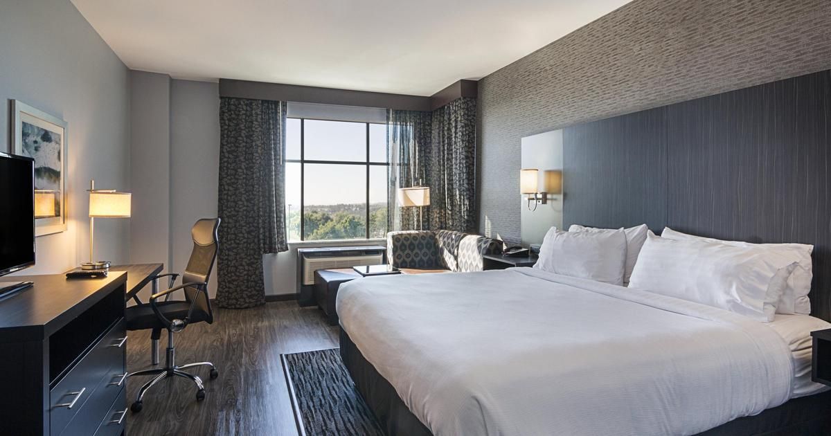 A hotel room with a king size bed , desk , chair and television.