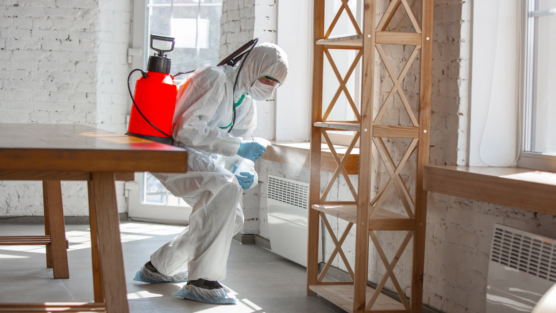 A man in a protective suit is cleaning a table in a room.