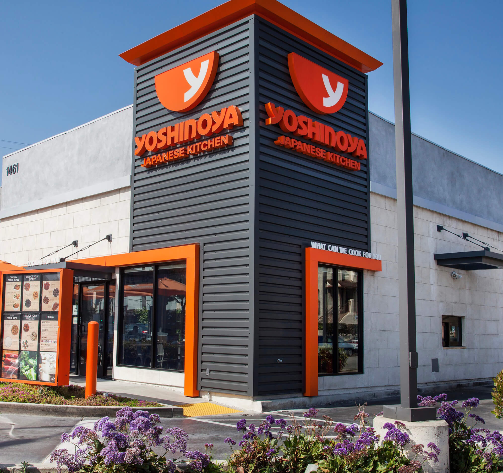 A yoshinoya restaurant with purple flowers in front of it