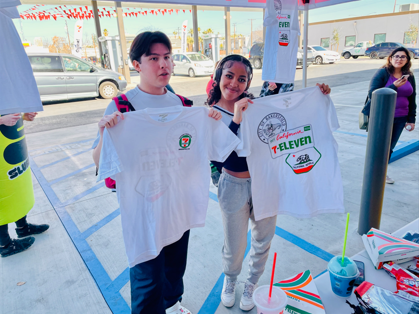 A boy and a girl are holding up t-shirts in a parking lot.