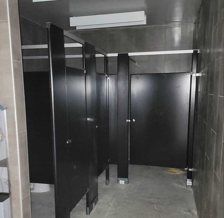 Public restroom with black stall doors and gray walls.