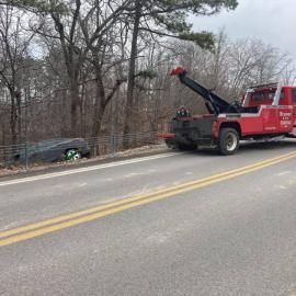 A red tow truck pulling a car out of a ditch alongside a road.