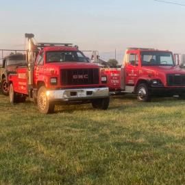 Two red tow trucks parked on grass.