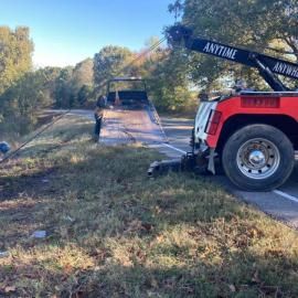 Tow truck loading a vehicle onto its flatbed on a roadside. The truck is red and black; the setting is outdoors.