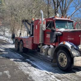 Red tow truck on snowy road with a person standing nearby.