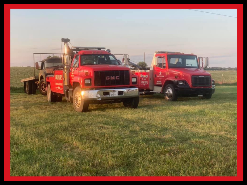 Two red tow trucks parked on a grassy field; one with a trailer.