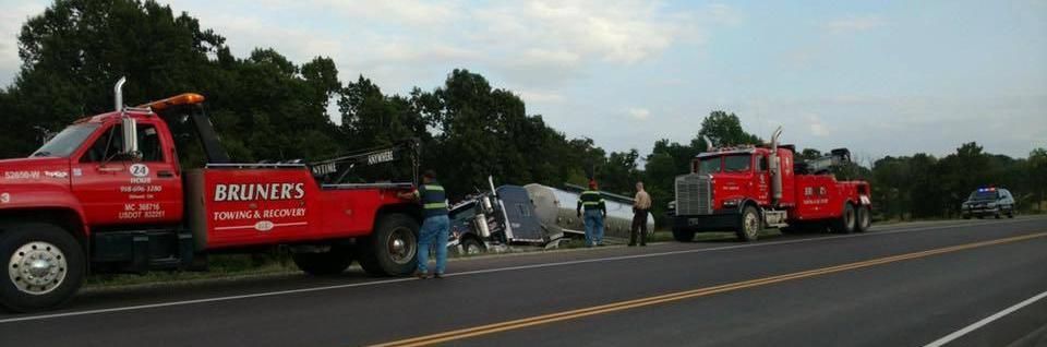 Tow trucks and a crashed tanker on a highway shoulder.
