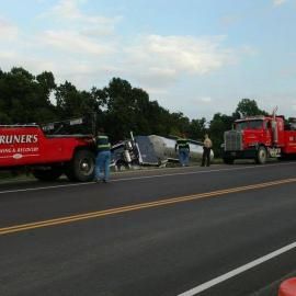 Two tow trucks at the scene of a semi-truck accident on a highway.