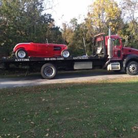 Red hot rod on a tow truck. Truck is red, in a grassy setting.