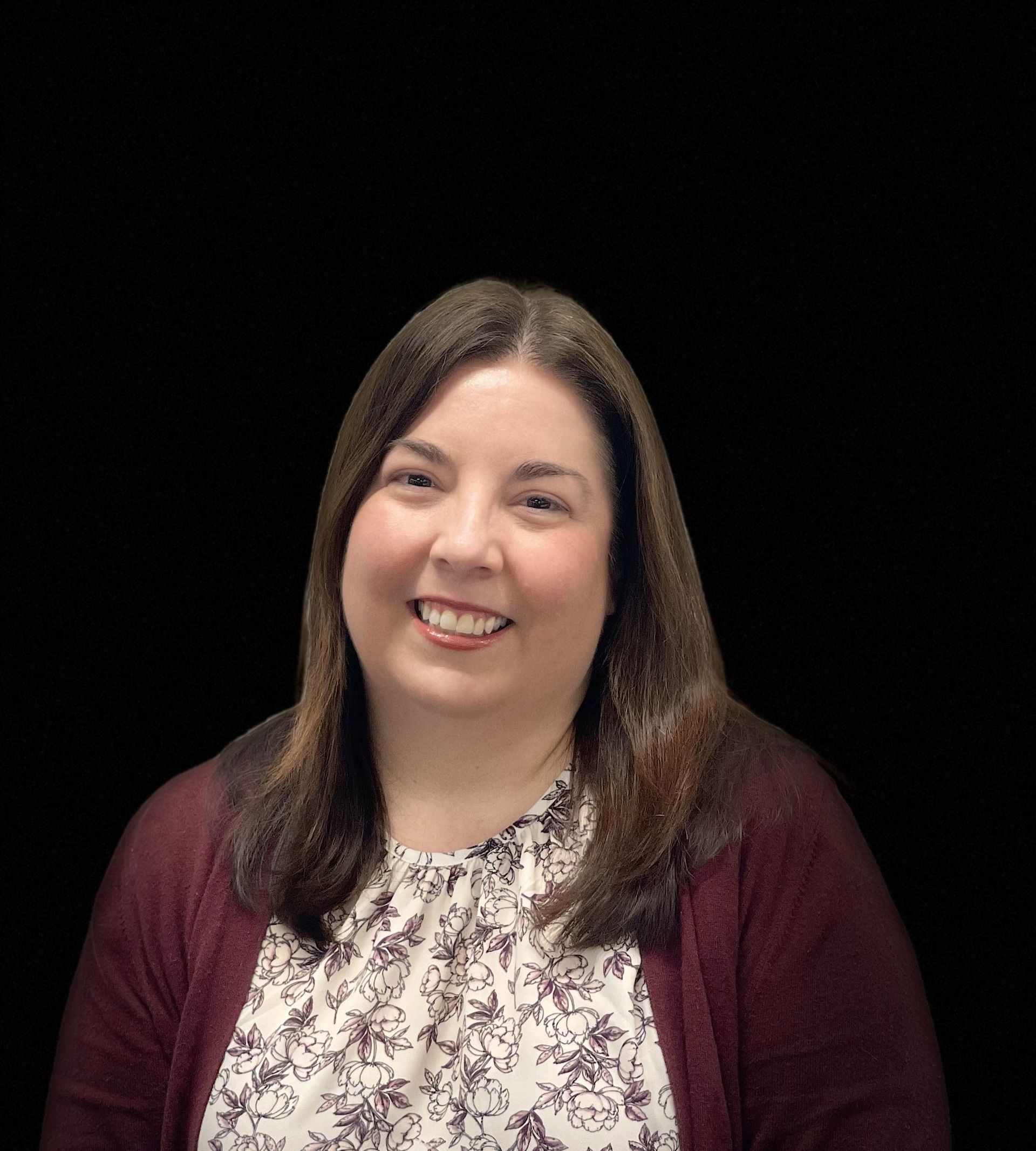 A woman is smiling for the camera while wearing a floral shirt and a maroon cardigan.