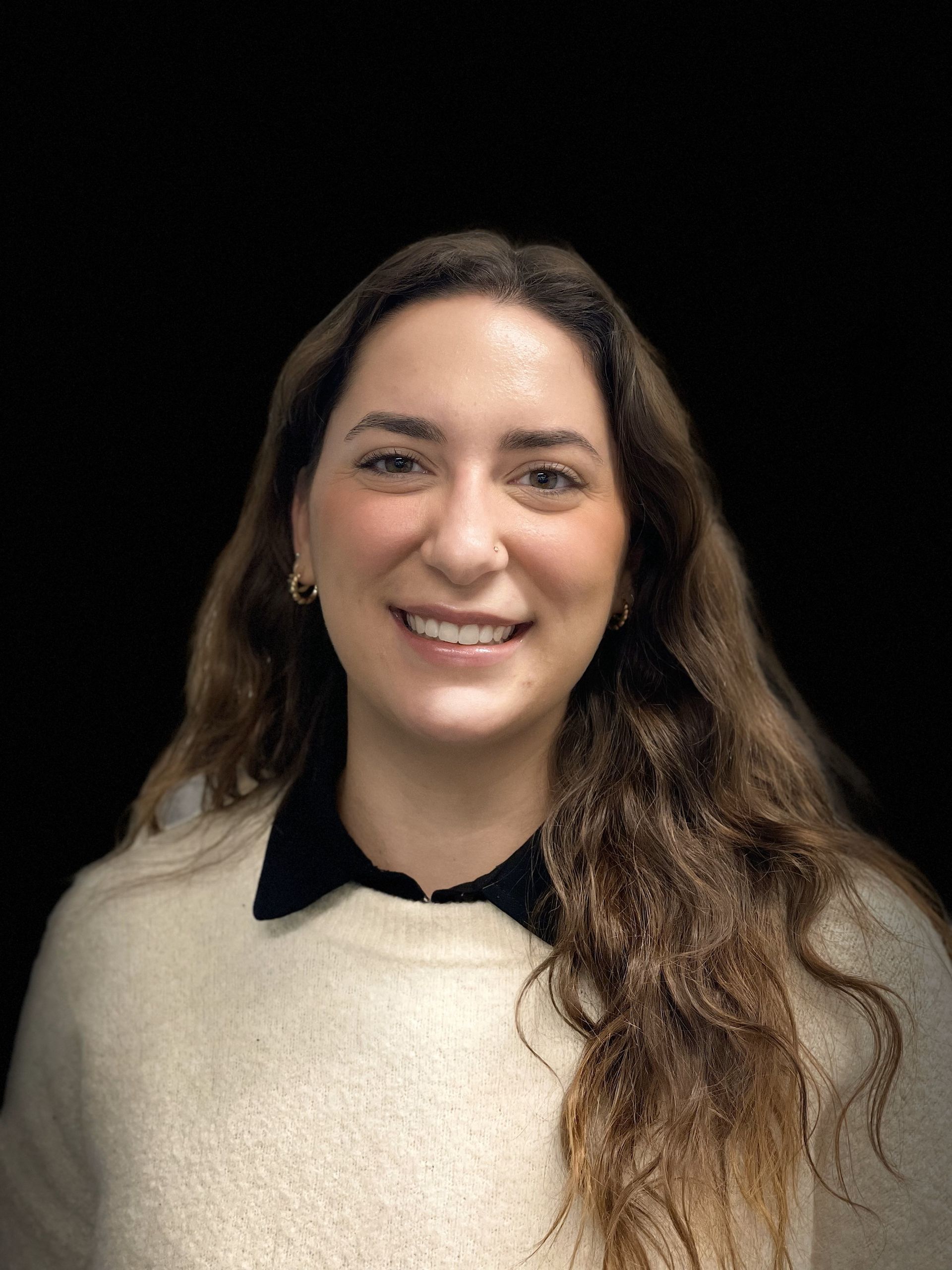 A woman wearing a white sweater and a black collar is smiling for the camera.